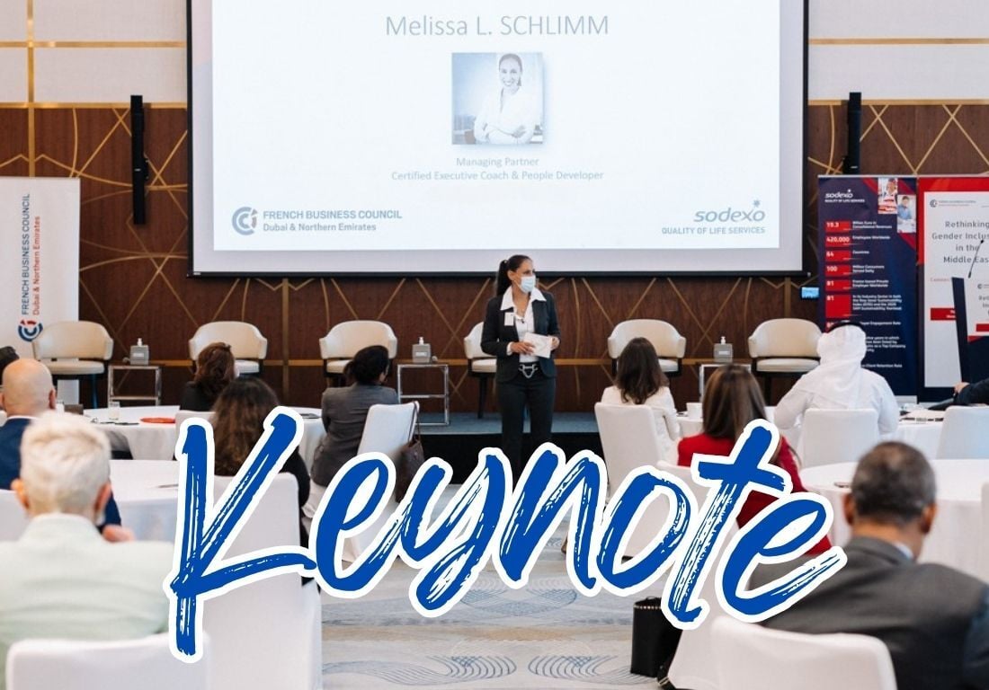 A photo of a woman (Melissa) standing on a stage with a microphone, speaking in front of an audience. A large screen behind her displays her name, the names of the organizers (French Business Council and Sodexo), and a photo of her. In the foreground, the word “Keynote” is written in large, blue, handwritten-style letters.